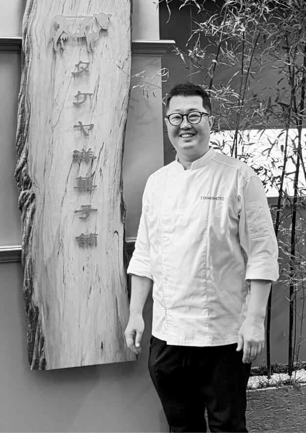 木の看板の前に立つシェフの山本健さん